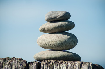 Closeup of stone balance on wooden fence on blue sky backgroundv