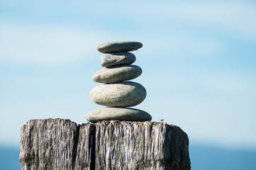 Closeup of stone balance on wooden fence on blue sky background