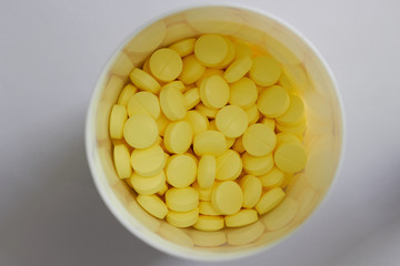 yellow round tablets in white plastic jar in medical healthcare drugstore concept,closed up