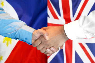 Handshake on Philippines and UK flag background.