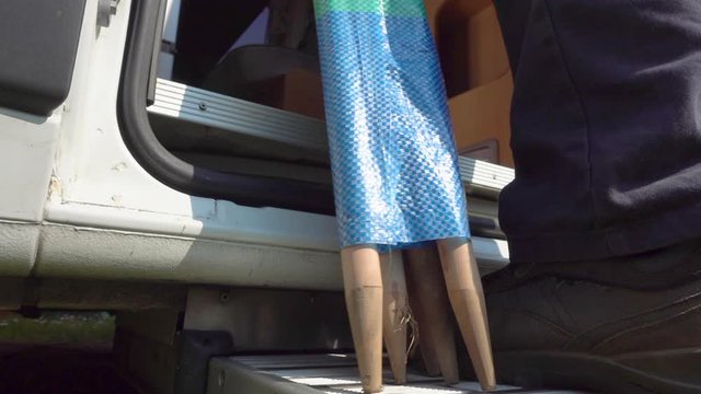 Slow motion close POV shot from ground level of a man&rsquo;s legs as he climbs up the step of a motorhome / campervan, carrying a rolled up windbreak with wooden poles, to take away on holiday / vacation.