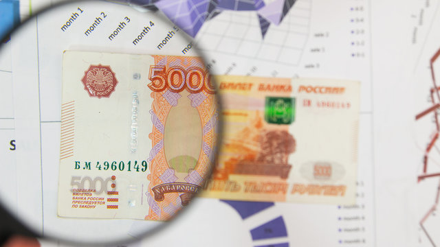 Magnifying glass and money - business background. Five thousand ruble bill under a magnifying glass is being inspected.