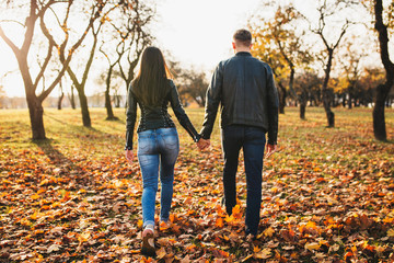 Slender athletic guy and girl go into the distance holding hands in the autumn forest