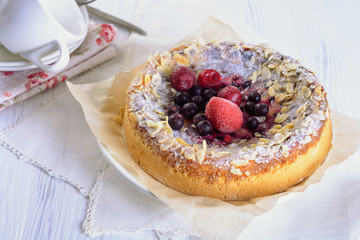 A delicious berry tarte (flan) next to tea cup on white wooden table