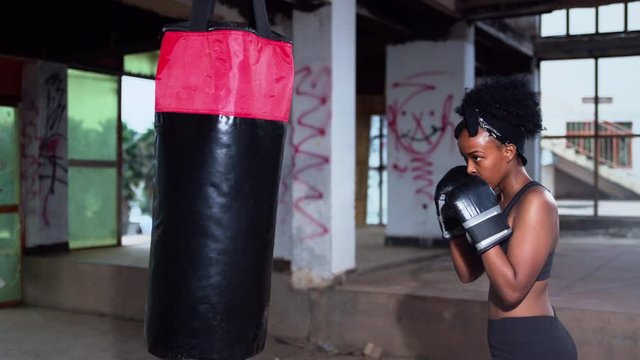  Young african Beautiful woman punching boxing bag during her training in warehouse