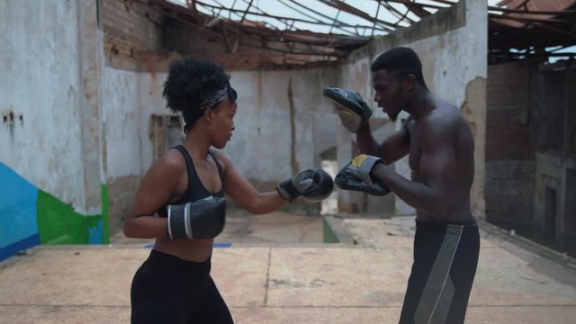 Young woman Athlete Is Engaged In Boxing With Her Coach african man in warehouse in the city 