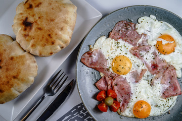 Bacon or ham and eggs in a plate high angle view by the fork knife and bread ready to eat served on...