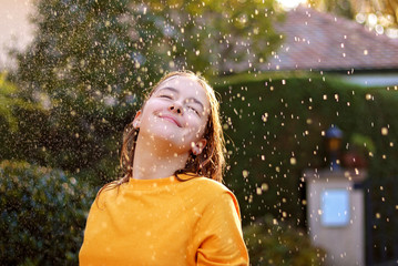 Happy smiling teenage girl enjoying rain and sun putting her face under water drops smiling happily...