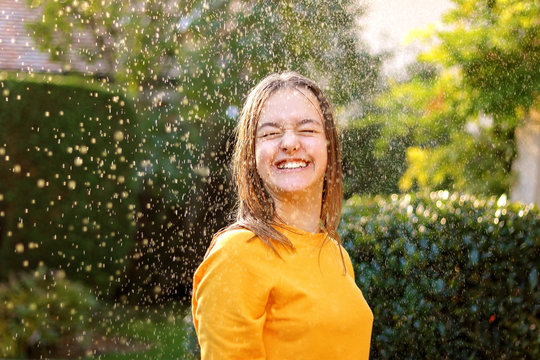 Happy smiling teenage girl enjoying rain and sun putting her face under water drops smiling happily and closing her eyes. True happiness. Summer lifestyle.