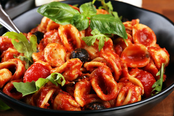 Pasta orecchiette. Plate of delicious orecchiette with tomato sauce garnished with parmesan cheese and basil on rustic background