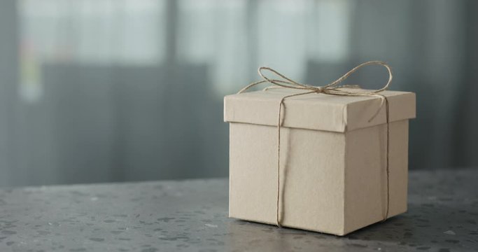 Slow motion man hand bring brown paper gift box on terrazzo countertop