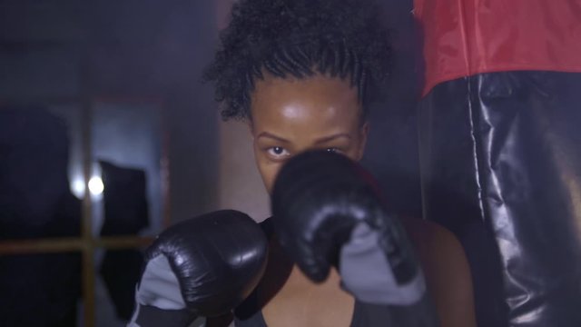 Portrait of a woman training his fist in huge smoke in the background near boxing bag 