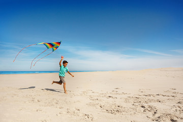 Little boy run alone with color kite on sea beach