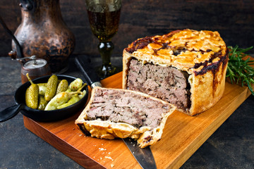 Traditional French Pate en croute with goose liver as closeup with gherkin and pepperoni on a modern design cutting board