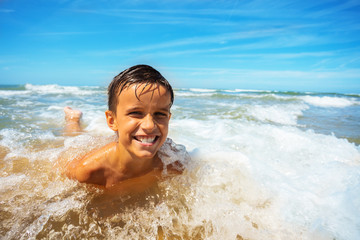 Happy smiling boy play in sea waves on a beach