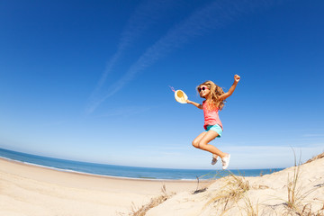 Obraz premium Happy little beautiful girl jump from sand dune