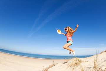 Happy little beautiful girl jump from sand dune