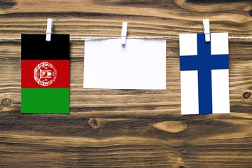Hanging flags of Afghanistan and Finland attached to rope with clothes pins with copy space on white note paper on wooden background.Diplomatic relations between countries. Cooperation concept.