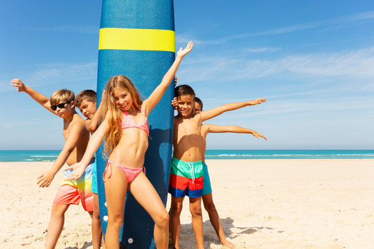 Group of kids stand near surfboard on the beach