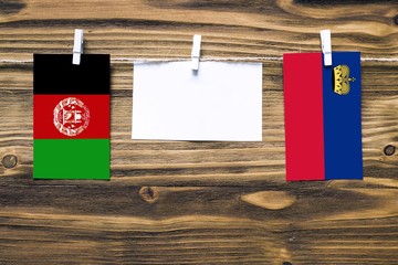 Hanging flags of Afghanistan and Liechtenstein attached to rope with clothes pins with copy space on white note paper on wooden background.Diplomatic relations between countries. Cooperation concept.