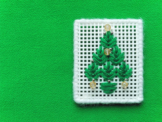 Handmade Christmas tree embroidered on white grid and decorated with beads on background of green tweed fabric. New Year and Christmas greeting card blank with copy space.