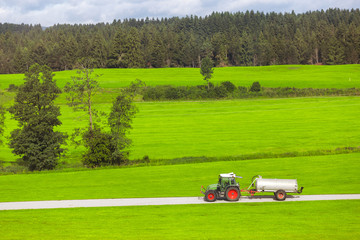 Tractor with fertilizer tank rides on a country road in a green field. Agriculture and farming...