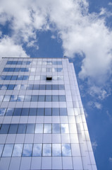 Fototapeta premium Architectural background, fragment of a modern office building against blue sky with clouds