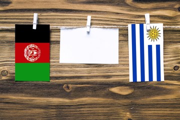 Hanging flags of Afghanistan and Uruguay attached to rope with clothes pins with copy space on white note paper on wooden background.Diplomatic relations between countries. Cooperation concept.
