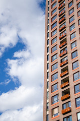 Architectural background of a fragment of orange modern residential building against the blue sky with clouds