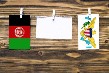 Hanging flags of Afghanistan and United States Virgin Islands attached to rope with clothes pins with copy space on white note paper on wooden background.Diplomatic relations between countries.