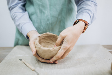 The potter's hands are shaped a cup from a clay. The process of creating pottery. The master ceramist works in his studio. Close-up, only hands. Crockery from clay own hands.