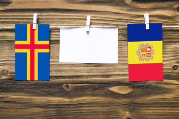 Hanging flags of Aland Islands and Andorra attached to rope with clothes pins with copy space on white note paper on wooden background.Diplomatic relations between countries.