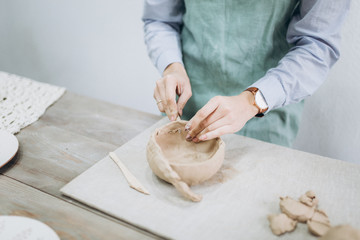 The potter's hands are shaped a cup from a clay. The process of creating pottery. The master ceramist works in his studio. Close-up, only hands. Crockery from clay own hands.