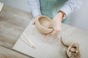 The potter's hands are shaped a cup from a clay. The process of creating pottery. The master ceramist works in his studio. Close-up, only hands. Crockery from clay own hands.