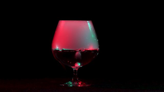 Dry ice bubbling in a cognac glass with smoke isolated on a black background with red light. Slow motion