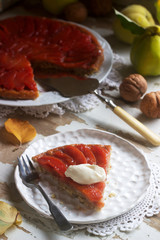 Quince tarte tatin served with whipped cream, quince fruits and walnuts on a wooden surface. Rustic style.