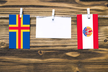 Hanging flags of Aland Islands and French Polynesia attached to rope with clothes pins with copy space on white note paper on wooden background.Diplomatic relations between countries.