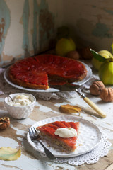 Quince tarte tatin served with whipped cream, quince fruits and walnuts on a wooden surface. Rustic style.
