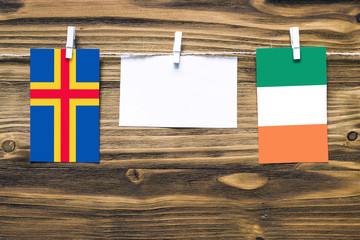 Hanging flags of Aland Islands and Ireland attached to rope with clothes pins with copy space on white note paper on wooden background.Diplomatic relations between countries.