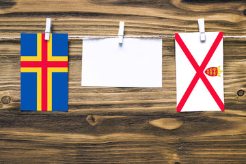 Hanging flags of Aland Islands and Jersey attached to rope with clothes pins with copy space on white note paper on wooden background.Diplomatic relations between countries.