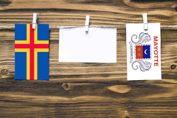 Hanging flags of Aland Islands and Mayotte attached to rope with clothes pins with copy space on white note paper on wooden background.Diplomatic relations between countries.