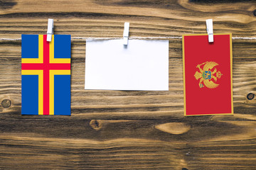 Hanging flags of Aland Islands and Montenegro attached to rope with clothes pins with copy space on white note paper on wooden background.Diplomatic relations between countries.