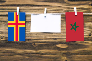 Hanging flags of Aland Islands and Morocco attached to rope with clothes pins with copy space on white note paper on wooden background.Diplomatic relations between countries.