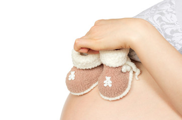 female hand holding knitted booties for newborn babies on white background of the pregnant belly, the concept of waiting for a child