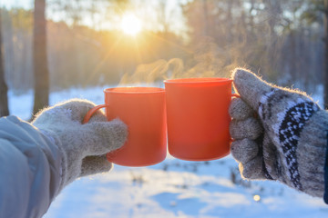 mugs with a hot drink of coffee or tea in the hands of people, a walk in the winter forest, a...