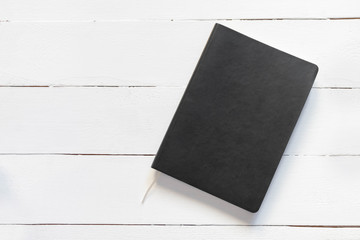 Black empty notebook on white wooden table. Image with copy space, top view