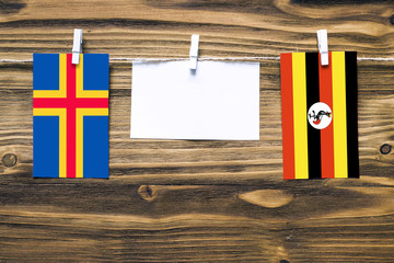 Hanging flags of Aland Islands and Uganda attached to rope with clothes pins with copy space on white note paper on wooden background.Diplomatic relations between countries.