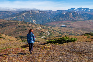 girl traveler on the edge of the cliff looking at the plain and mountains, green and orange hills, valley