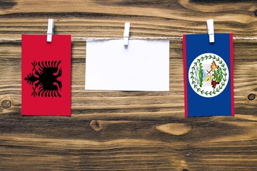 Hanging flags of Albania and Belize attached to rope with clothes pins with copy space on white note paper on wooden background.Diplomatic relations between countries.