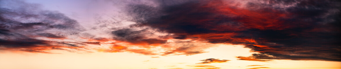 Sunset sky background in yellow red and dark tones. Wide angle panorama of gloomy sky, banner format